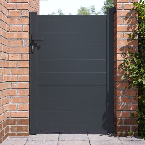 Dark gray metal gate mounted on a brick wall with greenery.