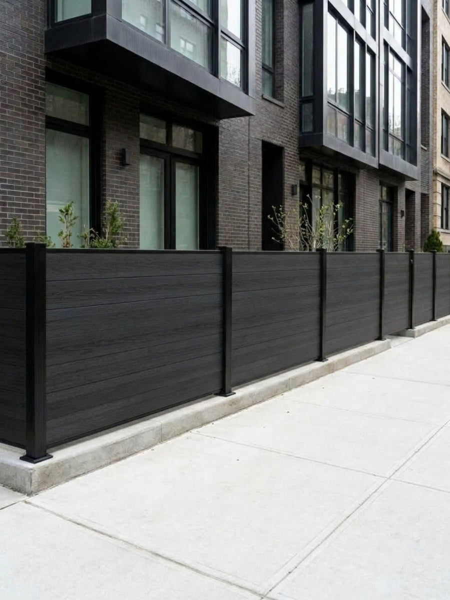 Row of black composite privacy fence panels lining the sidewalk outside a brick residence
