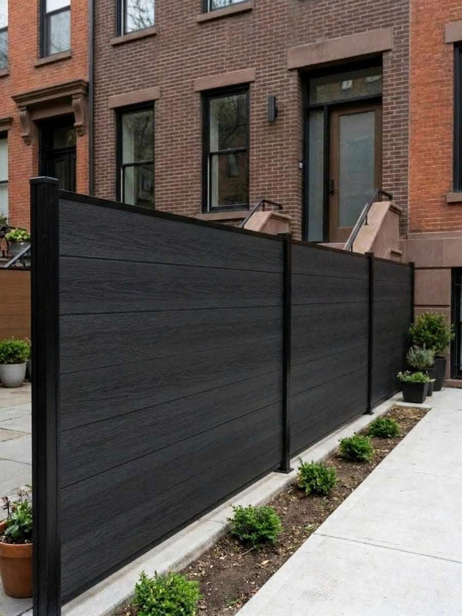 Black composite privacy fence panels with wood-grain texture installed beside a brick townhouse