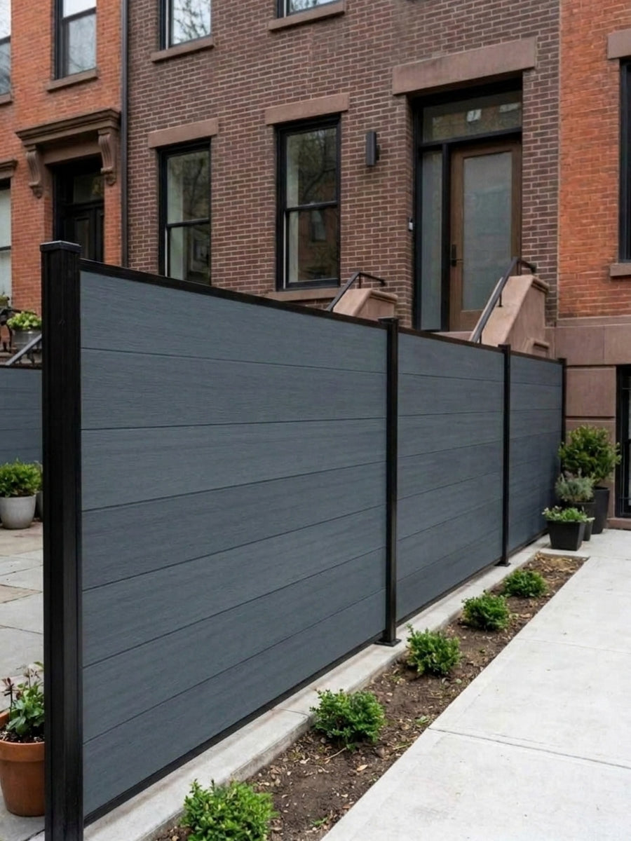 Light gray composite privacy fence panels with black posts lining a sidewalk beside brick townhomes