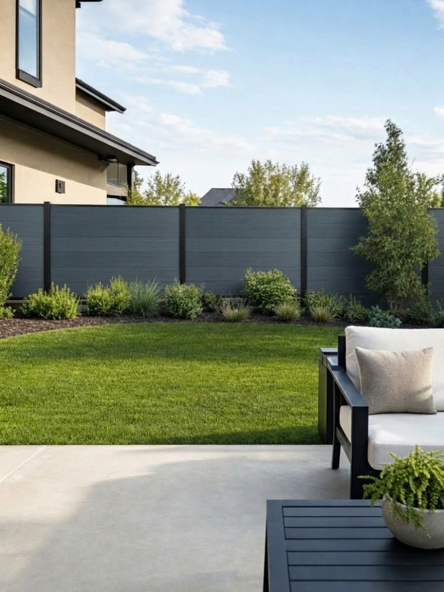 Light gray composite privacy fence panels installed around a landscaped backyard lawn and patio
