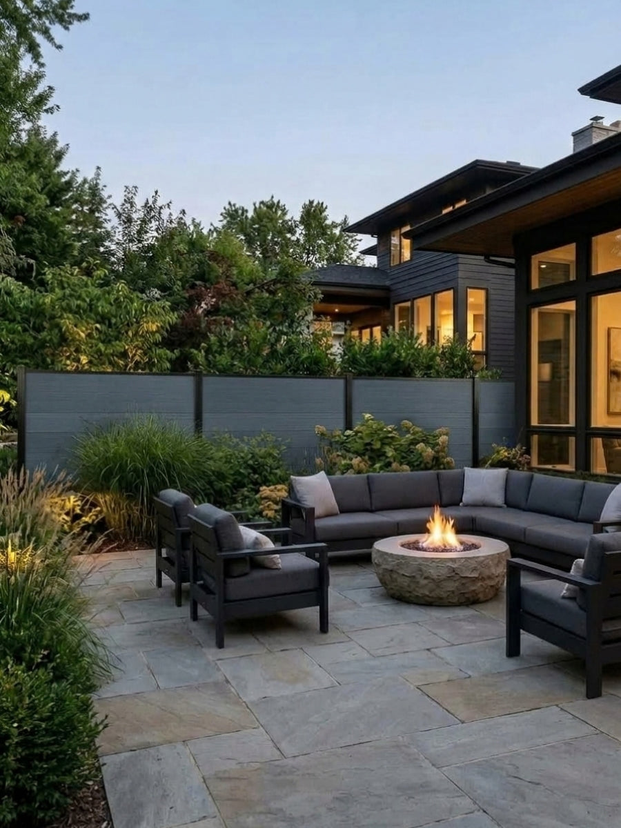 Light gray composite privacy fence bordering a landscaped stone patio with lounge seating and fire pit
