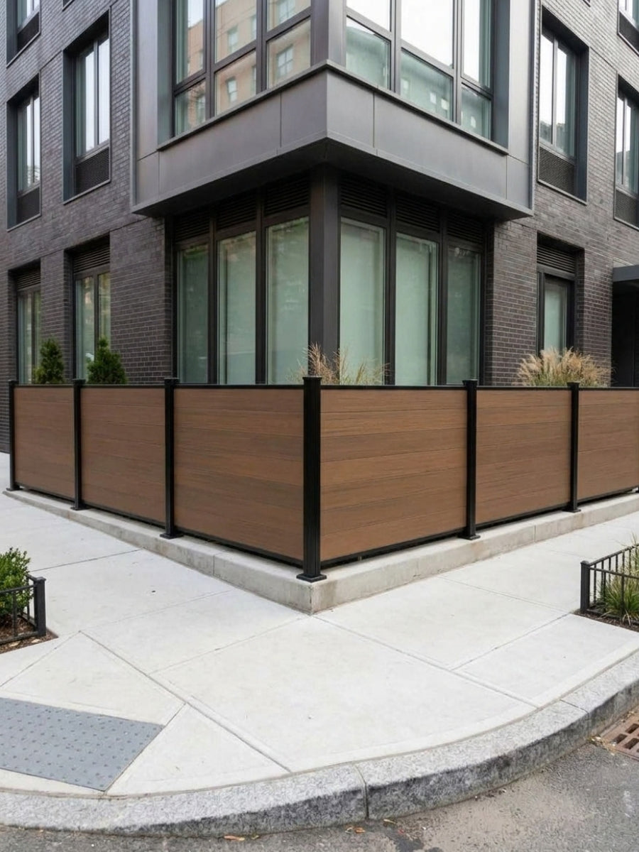 Walnut composite privacy fence panels installed around the corner of a dark brick building
