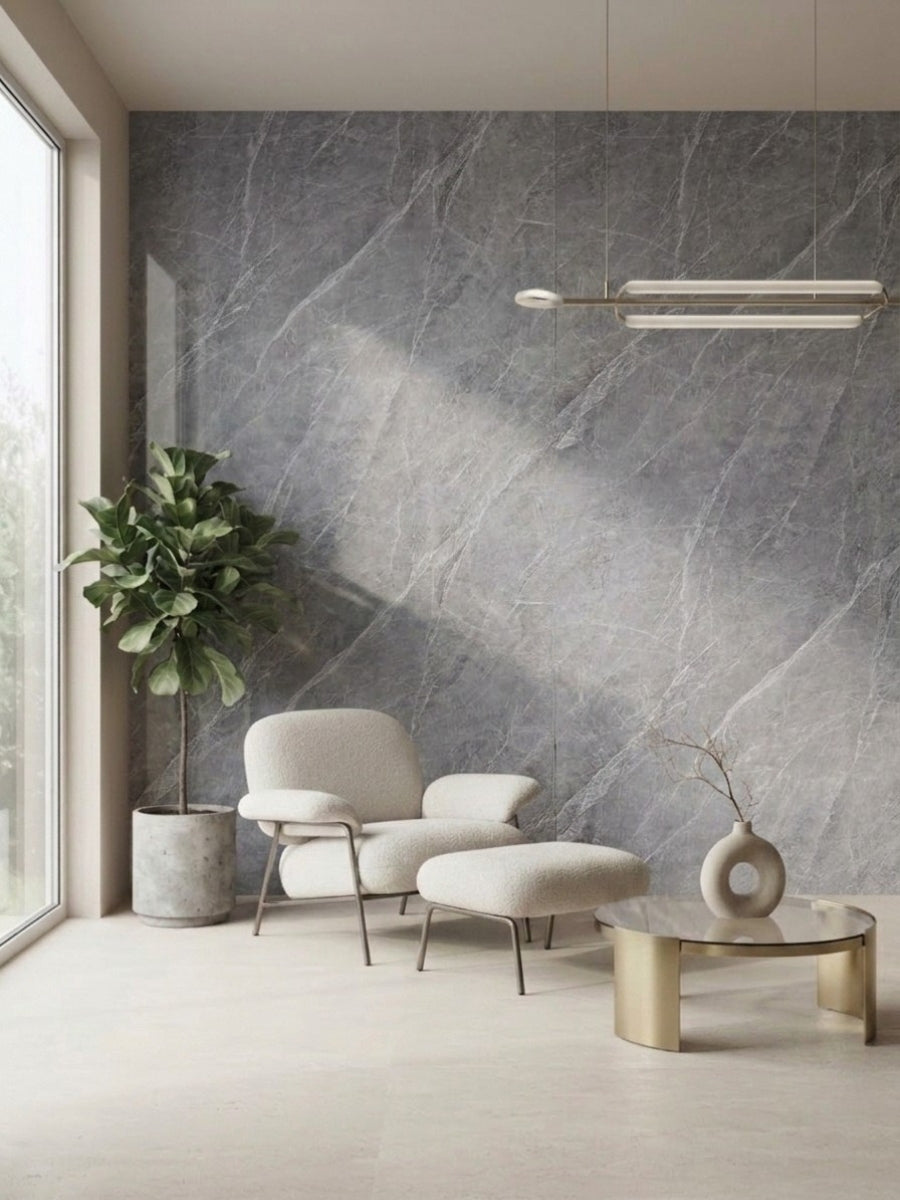 Ash gray marble-look PVC wall panel behind a cream lounge chair, ottoman, potted plant, and round coffee table.